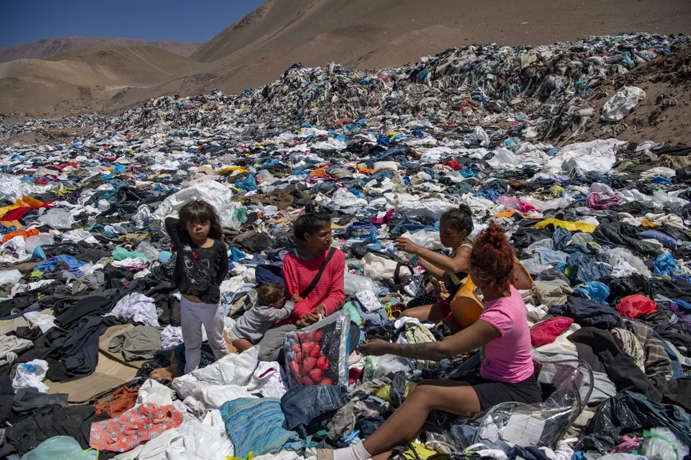 Mulheres buscam roupas usadas em meio a descarte no deserto do Atacama, em Alto Hospicio, — Foto: Martin Bernetti/AFP